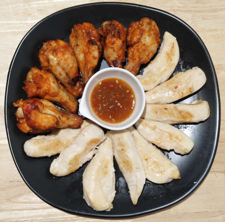 goup of slice of healthy grilled fresh chicken breast and fried chicken legs serving with spicy sauce on Black ceramic plate on wooden table, homemade restaurant, menu advertisement, food stylist backの写真素材