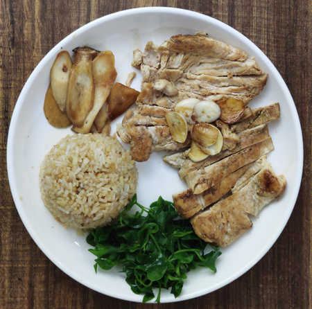 Overhead view of homemade toast and Sliced Grilled organic Chicken meat, steak topping with rice and green organic vegetable and grilled mushroom serving on white plate on wooden tableの写真素材