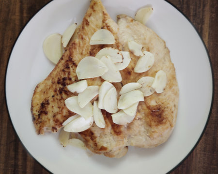 Overhead view of homemade toast and Sliced Grilled organic Chicken meat, steak topping with sliced garlic serving on white plate on wooden table, One famous healthy meal menu of secret recipe restauraの写真素材
