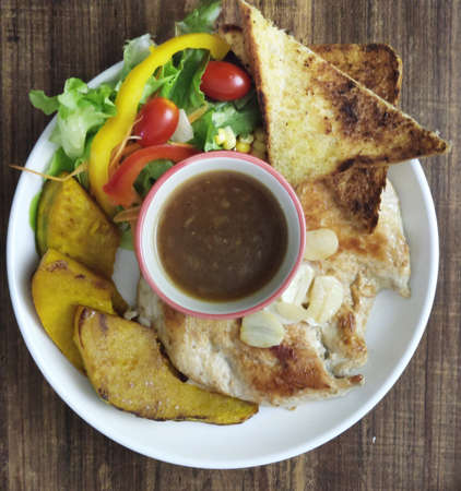 Overhead view of homemade toast and Sliced Grilled organic Chicken meat, steak serving with bread and colorful salad pumpkin and gravy sauce on white plate on wooden table, One famous healthy meal ofの写真素材