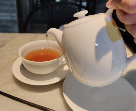 Tea party time. Hostess pours tea into white ceramic cups on festive table. Focus on tea pictures for advertisemenの写真素材