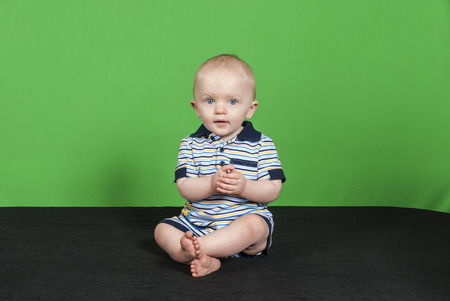 10 Month Old Happy Baby Boy on a Green Background Playing with his Handsの写真素材