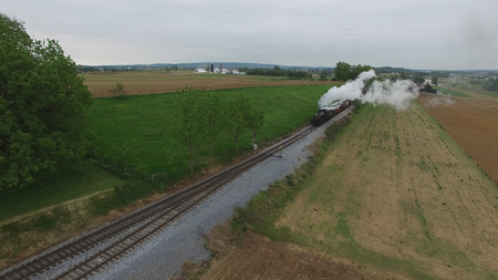 Aerial View of a Steam Passenger Train Puffing Smoke in Amish Countryside on a Sunny Spring Dayの写真素材