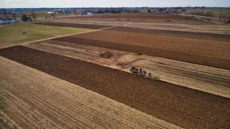 Aerial View of Amish Farm Worker Turning the Field in Early Spring as Seen by a Droneの写真素材