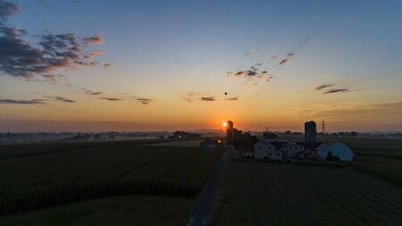 An Aerial View of a Sunrise Over an Amish Farm with Blues and Reds With a Hot Air Balloon Floating...