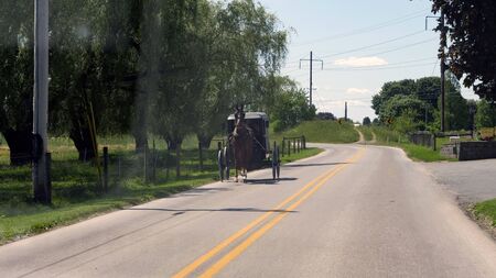 View of an Amish Horse and Buggy Going down the Road on a Sunny Dayの写真素材