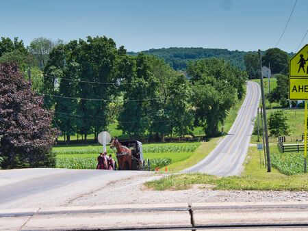 Amish Teenagers Walking Along Train Tracks with a Horse and Buggy Approaching in Countryside on a Sunny Dayの写真素材