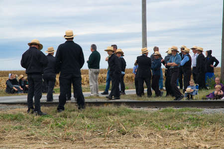 Strasburg, Pennsylvania, October 2019 - Group of Amish men women and children patiently wait for a train to pass along train tracks on a fall day.のeditorial素材