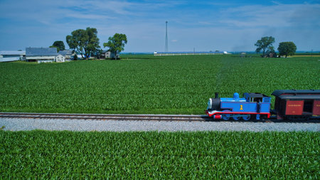 Ronks, Pennsylvania,June 2019 - Aerial View of Thomas the Tank Engine Approaching Thru Trees and Farmlands Pulling Passenger Cars Blowing Smoke on a Beautiful Summer Dayのeditorial素材