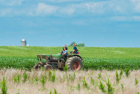 Ronks, Pennsylvania, July 2021 - Amish Boy and Girl Teenagers Riding on a Old Tractor Thru Farmlands...