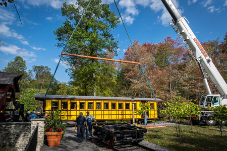 Elizabethtown, Pennsylvania, October 7, 2020 - Installing a New Yellow Passenger Antique Coach Being Lifted By a Crane to install on Train Trucks on to a Railroad Track on a Fall Dayのeditorial素材