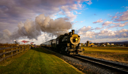 A View of a Classic Steam Passenger Train Approaching, With American Flags Attached to a Fence on a Sunny Autumn Dayの写真素材