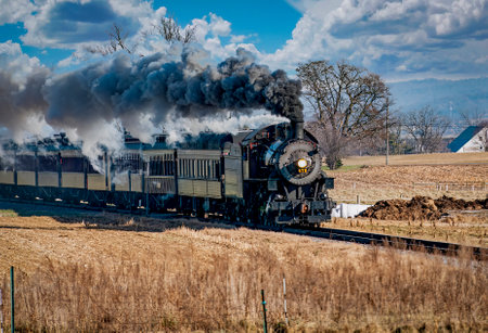Ronks, Pennsylvania, December 28, 2022 - A View of a Classic Steam Passenger Train Approaching, Traveling Thru the Countryside, Blowing Smoke and Steam on a Winter Dayのeditorial素材