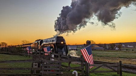 A View of an Antique Stream Passenger Train, Traveling at Sunrise, While passing a Fence with...