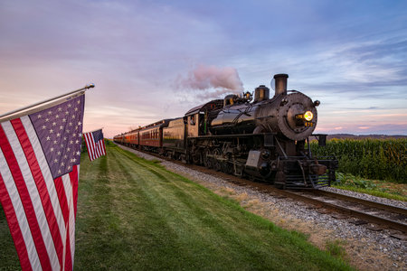 Ronks, Pennsylvania, August 19, 2022 - Classic Steam Passenger Train Approaching, With American Flags Attached to a Fence on a Sunny Summer Dayのeditorial素材