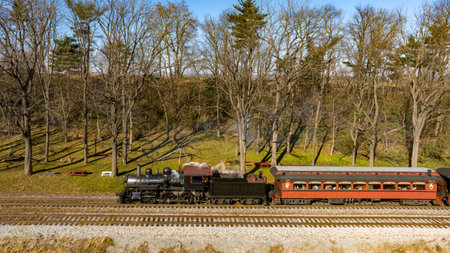 A Drone View of a Restored Steam Passenger Train Traveling Thru Farmlands Pulling Up to a Small Station on an Autumn Dayの写真素材