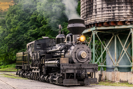 Cass, West Virginia, June 18, 2022 - An Antique Shay Steam Locomotive, Steamed up, Blowing Smoke, Sitting by a Water Tower, Getting Ready for Workのeditorial素材