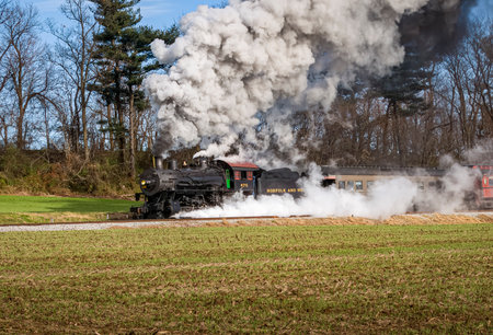 Ronks, Pennsylvania, December 4, 2022 - A View of a Classic Steam Passenger Train, Blowing Lots of Smoke and Steam, While Traveling in the Countryside on an Autumn Dayのeditorial素材