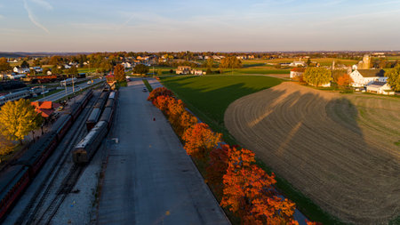 An Aerial View of a Train Station with a Row of Autumn Trees, in Red and Orange on a Sunny Autumn Morningの写真素材