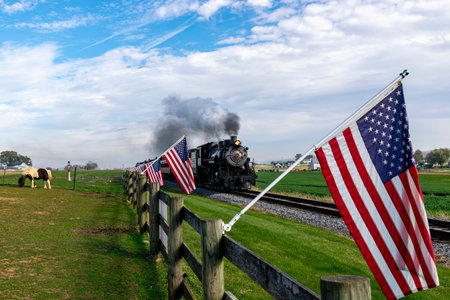Ronks, Pennsylvania, November 4, 2023 - View of an Antique Steam Passenger Train Approaching With a Line of American Flags, Blowing Smoke on a Fall Dayのeditorial素材