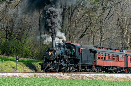 Strasburg, Pennsylvania, April 4, 2023 - An Angled View of a Restored Steam Passenger Train Moving Slowly Blowing Lots of Black Smoke and White Steam on a Sunny Dayのeditorial素材