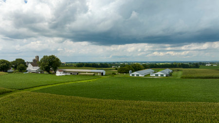 A peaceful farming homestead lies under a dramatic sky, where the dense clouds hint at the changing weather over the lush landscape.の写真素材