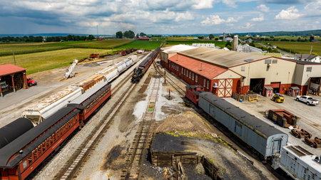 Strasburg, Pennsylvania, August 15, 2023 - Captured from above, a bustling railway junction services a mix of passenger and freight cars, framed by the lush farmland it supports.のeditorial素材