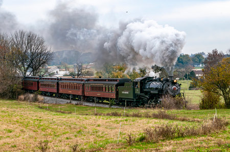 Ronks, Pennsylvania, November 4, 2023 - A steam train is traveling through a field. The smoke from...