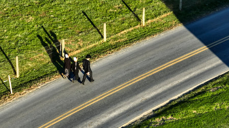 Ronks, Pennsylvania November 14, 2023 - A trio of Amish, walk along a country road, casting long shadows in the afternoon sun, perfect for lifestyle and community themes.のeditorial素材