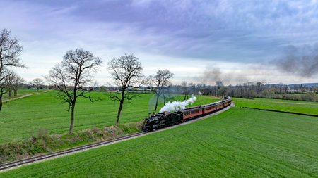 Dramatic aerial capture of a vintage steam train chugging along a curvy track through lush green...