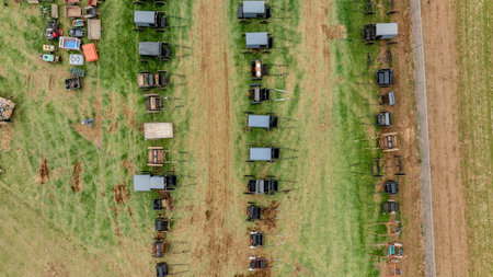 Aerial View Of Neatly Aligned Horse-Drawn Buggies And Carts On Grass, With Various Agricultural Equipment On The Side, Highlighting A Rural Setting With Well-Trodden Pathways.の写真素材