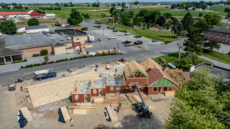 Bird in Hand, Pennsylvania, USA, June 4, 2024 - Aerial View Of A Busy Construction Site With Wooden Framing And Building Materials On A Sunny Day, Surrounded By Green Fields, Residential Buildings, And Vehicles Parked In A Nearby Lot.のeditorial素材