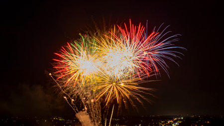 Brilliant Red, Green, And White Fireworks Burst In The Night Sky, Creating A Vibrant And Festive Atmosphere Over The Illuminated City Below.の写真素材