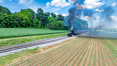 A Black Steam Locomotive Billowing Thick Smoke Pulls Red Passenger Cars Through Lush Green Fields...