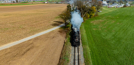 A vintage steam train chugs along grassy fields and farmland, surrounded by vibrant autumn colors.の写真素材