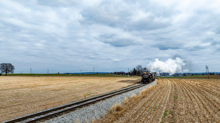A historic steam train chugs along the tracks, billowing white smoke as it cuts through open fields...