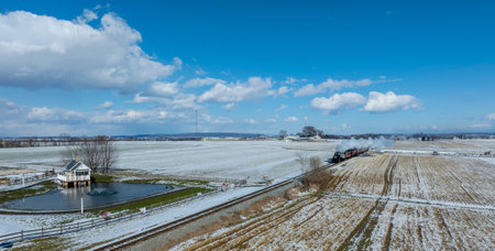 A steam locomotive chugs along the tracks, releasing vapor as it moves through snow-covered fields....
