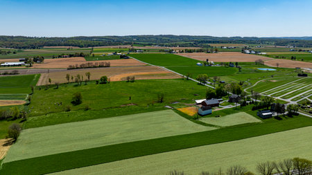 The landscape showcases sprawling fields of vibrant green grass and various crops, interspersed with...