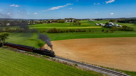 A vintage steam locomotive chugs along the railway, emitting black smoke against a backdrop of...