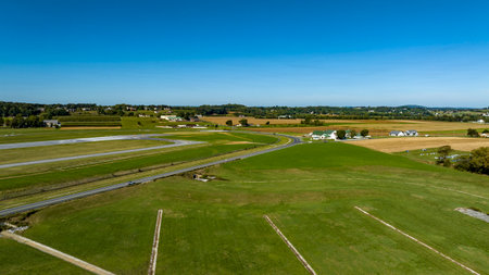A sweeping view of lush green fields stretching towards the horizon, interspersed with winding roads and small white houses. The landscape reflects a sunny, cloudless day in the countryside.の写真素材