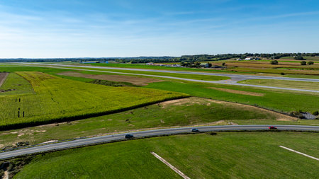 An expansive view showcases vibrant green fields of farmland alongside a small airstrip. The landscape is serene, with a clear blue sky enhancing the rural charm of the area.の写真素材