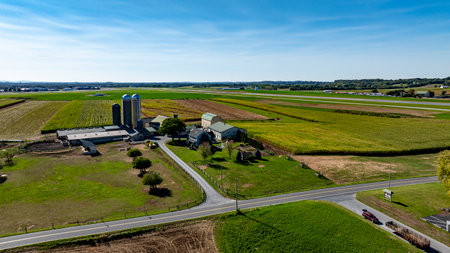 Sunny farmland stretches across the landscape, featuring green and golden fields. A farmhouse and...