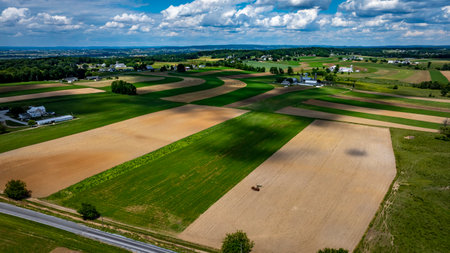 Vast agricultural fields dominate the landscape, showcasing a mix of green crops and brown earth.の写真素材