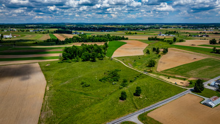 Green and golden fields stretch across the countryside, with a collection of farming buildings in...