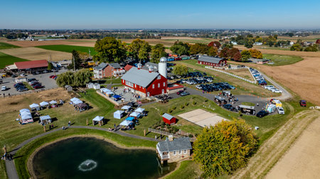 Ronks, Pennsylvania, USA, October 20 2024 - Visitors gather at a farm event featuring tents and activities around a pond, surrounded by picturesque fields and buildings under clear blue skies.の写真素材