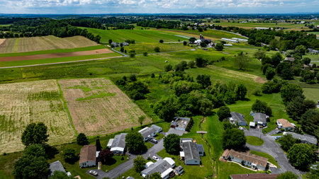 Aerial view of a tranquil rural community featuring various Mobile, Prefab, Manufactured houses situated near lush green fields and trees. The landscape shows harmonious blend of residences farmland.の写真素材