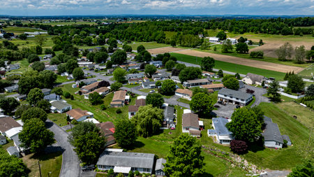 Aerial view of a tranquil rural community featuring various Mobile, Prefab, Manufactured houses situated near lush green fields and trees. The landscape shows harmonious blend of residences farmland.の写真素材