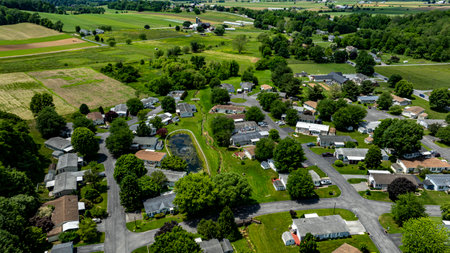 Aerial view of a tranquil rural community featuring various Mobile, Prefab, Manufactured houses situated near lush green fields and trees. The landscape shows harmonious blend of residences farmland.の写真素材