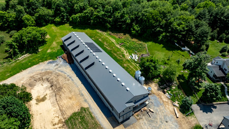 A large agricultural building with solar panels is being constructed in a rural setting. The site is surrounded by greenery and features open land, indicating future agricultural use.の写真素材