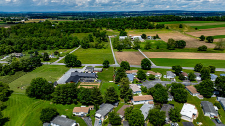 Aerial view of a tranquil rural community featuring various Mobile, Prefab, Manufactured houses situated near lush green fields and trees. The landscape shows harmonious blend of residences farmland.の写真素材